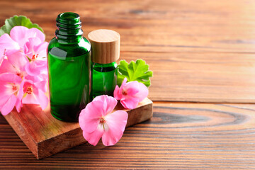 Geranium essential oil in bottles and beautiful flowers on wooden table, space for text