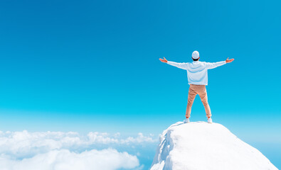 Naklejka premium Man stands on a snowy peak with arms outstretched under a clear blue sky