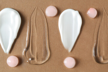 Smears of different cosmetic products on brown background, flat lay