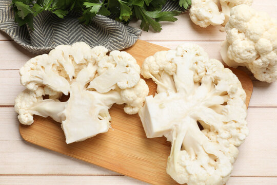 Uncooked cauliflower steaks and parsley on wooden table, flat lay