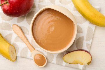 Delicious baby food in bowl and ingredients on white wooden table, flat lay