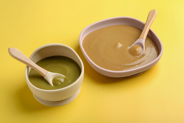 Delicious baby food and spoons in bowls on yellow table
