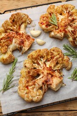 Tasty cauliflower steaks, rosemary and garlic on wooden table, top view