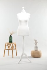 One female mannequin on stand, stool, pouf and vases with plants against light background