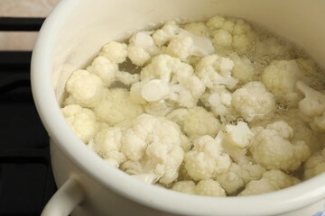 Cooking cauliflower. Florets in white pot with water on cooktop, closeup
