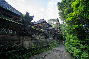 Cracked pavement footpath next to Pura Gunung Lebah temple marks the beginning of the Campuhan Ridge Walk in Ubud, Bali, Indonesia. Moss covered concrete walls and jungle on either side.