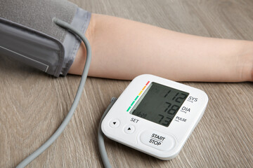 Woman measuring blood pressure at wooden table, closeup