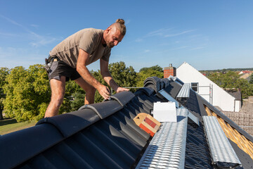 Ein Dach wird neu gedeckt. Beton-Dachsteine in der Farbe Anthrazit. Befestigung der Firstziegel