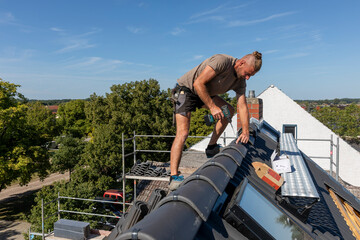 Ein Dach wird neu gedeckt. Beton-Dachsteine in der Farbe Anthrazit. Befestigung der Firstziegel