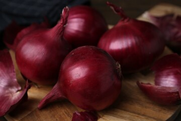 Fresh onions with peels on wooden board, closeup