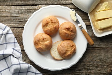 Plate with homemade tasty buns, butter and knife on wooden table, flat lay