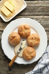Plate with homemade tasty buns, butter and knife on wooden table, flat lay
