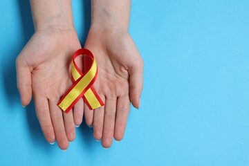 Woman with yellow and red ribbon on light blue background, top view with space for text. Hepatitis C awareness