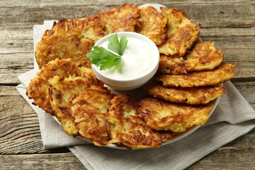 Delicious potato pancakes, sour cream and parsley on wooden table, closeup