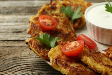 Delicious potato pancakes, sour cream, tomatoes and parsley on wooden table, closeup