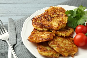 Delicious potato pancakes with tomatoes and parsley served on gray wooden table, closeup
