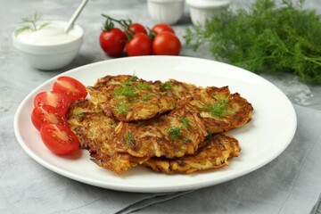 Delicious potato pancakes with fresh tomatoes served on grey table, closeup