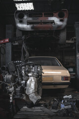 Engine on the crane and classic cars on a ramp in a background in the garage.