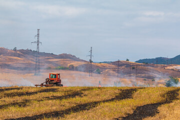 Fototapeta premium A burnt field after harvest. A red tractor plowing. Nagorno-Karabakh, Azerbaijan.