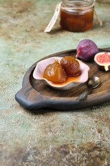 Fig jam in a pink bowl on a wooden tray on a green concrete background. Georgian cuisine.