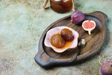 Fig jam in a pink bowl on a wooden tray on a green concrete background. Georgian cuisine.