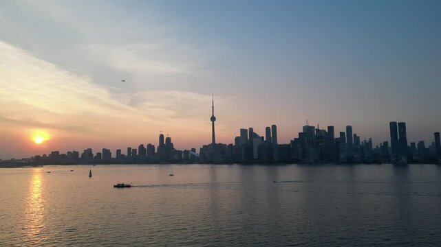 Sunset behind downtown Toronto waterfront skyline aerial view above the harbor showing the entire city shoreline including the famous CN tower. Drone flying slowly back and to the left