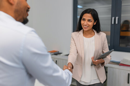 Indian female hiring manager shaking hands with an African American male candidate at the end of a successful job interview.