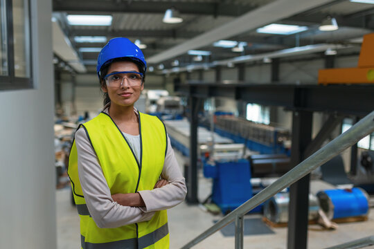 Female industrial plant employee with a blue helmet and yellow vest in a business factory. Manufacturing, labor, and women concepts.