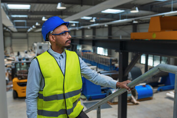 Man with a blue helmet and yellow vest, a worker in a factory unit checking a work process,...