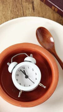 Alarm clock in empty plate with spoon and holy bible book. Top view. Vertical video. Christian fasting concept.