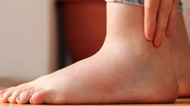 Female hand is massaging swollen foot at home. Close-up. Edema pain, physical therapy, wounded muscle, leg injury, and health care concept.