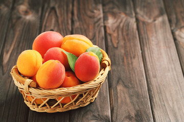 Sweet apricots with leaves in basket on wooden background
