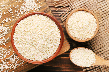 Sesame seeds in spoon and bowls with cutting board and sackcloth on wooden background