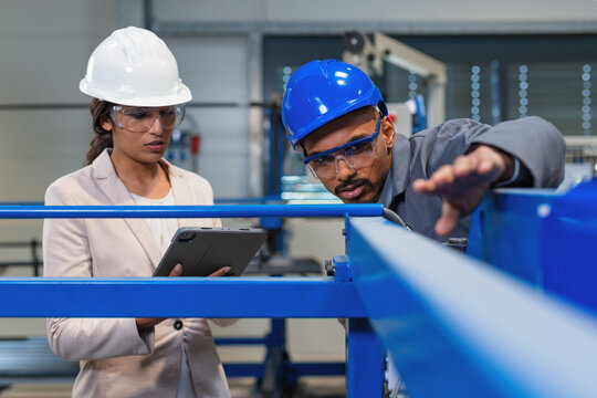 African American engineer and an Indian woman a factory manager holding a tablet, walking through the production line, doing inspection, front view.