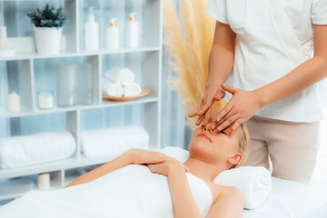 Caucasian woman enjoying relaxing anti-stress head massage and pampering facial beauty skin recreation leisure in dayspa modern light ambient at luxury resort or hotel spa salon. Quiescent