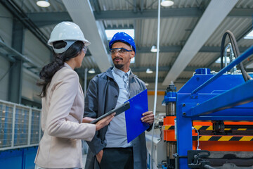African American engineer and an Indian woman a factory manager holding a tablet, walking through...