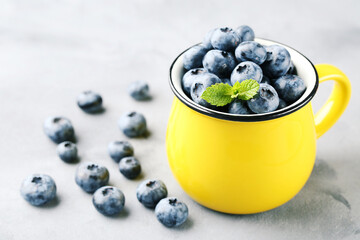 Blueberries with mint leafs in yellow mug on grey background