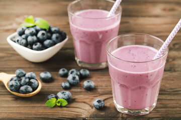 Blueberries and glasses of smoothie and green leafs on wooden background