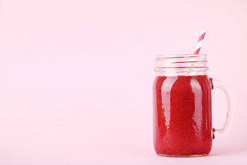 Red smoothie in glass jar on pink background