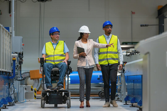 Production manager, a woman, walking alongside two workers in the factory, one of whom with a disability. Diversity in work concept.