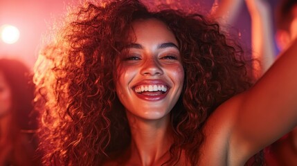 A cheerful woman with curly hair laughs and enjoys herself surrounded by a lively crowd in a vibrant and festive club ambiance with glowing lights.