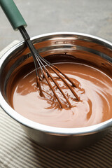 Chocolate dough and whisk in bowl on grey table, closeup