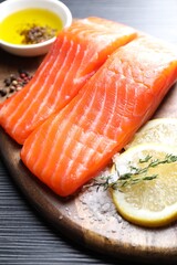 Pieces of fresh salmon with thyme, lemon, oil and spices on black table, closeup