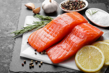 Pieces of fresh salmon with peppercorns, rosemary and garlic on dark textured table, closeup