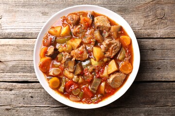 Delicious stew with vegetables in bowl on wooden table, top view