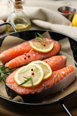 Fresh raw salmon steaks with spices in pan on wooden board, closeup