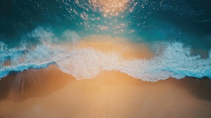 Top view of a beautiful blue ocean with sunlight sparkling on the waves and a golden sandy shore from a drone
