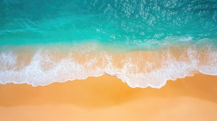 Top view of a sunny coastline with bright blue sea water and gentle waves lapping onto soft, golden sand