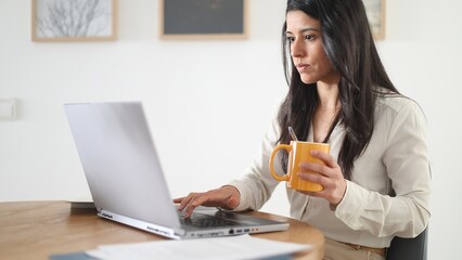 Focused businesswoman working from home drinking coffee and using laptop computer