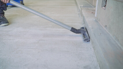 Construction worker vacuuming dust on concrete floor.